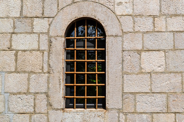 Fototapeta na wymiar Window with a lattice in the stone wall of the old fortress