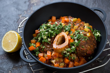 Osso buco stewed with vegetables and served with gremolata in a cast-iron pan, selective focus, horizontal shot