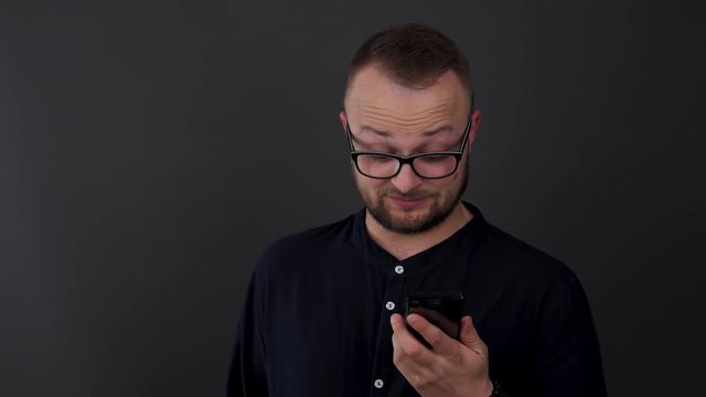 A young, bearded man with glasses. Studio shot of male disparagingly reacts to what he saw on his phone.