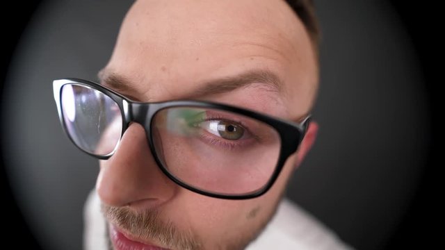 A young, bearded man with glasses looking in peephole. Mistrustful, surprised look.