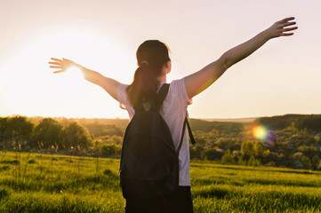 Young female with backpack standing outdoors against the sunset. Concept of the travelling, backpacking, hiking, otdoor recreation, success, inspiration