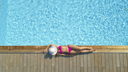 AERIAL: Attractive female tourist in pink bikini sunbathes in tropical summer.
