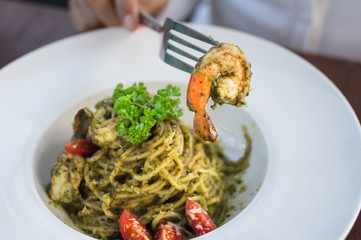 Girl eating green pesto sauce and shrimp spaghetti.