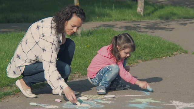 The family draws. A child with mother is painting with chalk on the asphalt.