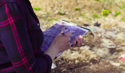 Close up hands of woman ecologist during the research on garbage dump. She marking something on the map.