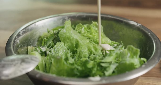 Slow motion closeup mixing frillis salad leaves with caesar sauce