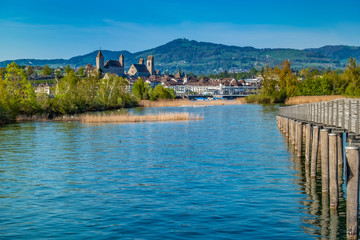 Fototapeta premium The Holzsteg, a wooden pedestrian bridge crossing the Zurich Lake (Obersee) Part of the eastern branch of the Way of Saint James. The Rapperswil castle is in the background. Switzerland