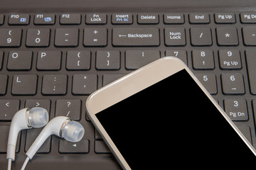 A smart phone and earphone on the keyboard