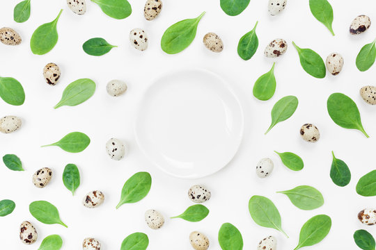 Empty plate, organic spinach leaves and quail eggs for a healthy recipe on white background top view. Flat lay.