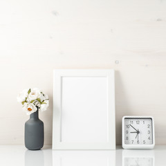White frame, flower in vase, clock on white table against the wh