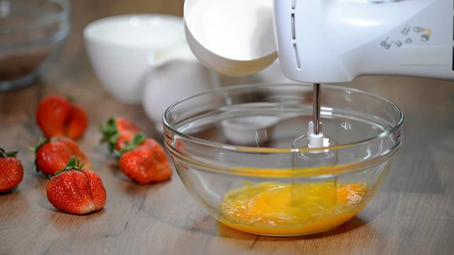 Beaten Eggs with Mixer Whisks in Bowl. Sugar being pouring into bowl.