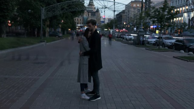 Couple hug and stay without moving on the street in evening time. Smashed crowd of people passing by. Time lapse.