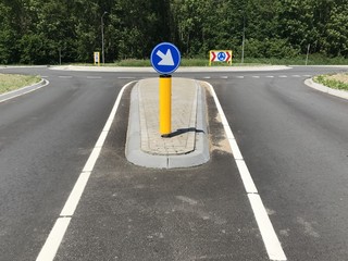Yellow Dutch traffic column with driving direction in front of a roundabout