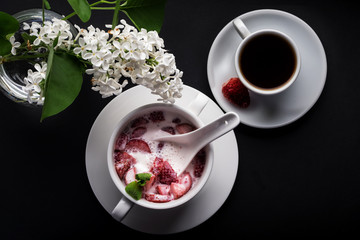 Dessert, strawberry with cream and mint slice, white plate, cup of coffee, black background, top view