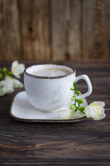 White cup of coffee cappuccino and white freesia flower on a wooden background. Free space, vertical photo