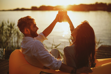 Young happy couple enjoy in beer by the river during the sunset