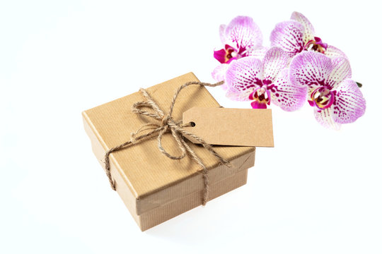 Orchid pink flowers and a gift box with a blank tag isolated on white background, copy space