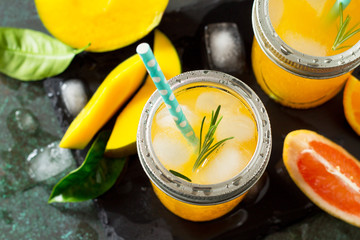 Refreshing summer cocktails made of citrus and mango, cold drink or a drink with ice on a dark stone background. Concept of vegetarian food, fresh vitamins.