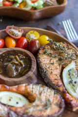 Salmon steak grilled on wooden plate with vegetables and sauce