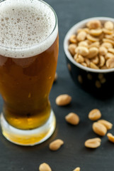 glass of beer and bowl with roasted and salted peanuts on slate social drinking concept