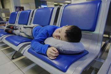 Tired little boy sleeping on chair while waiting flight at the airport.