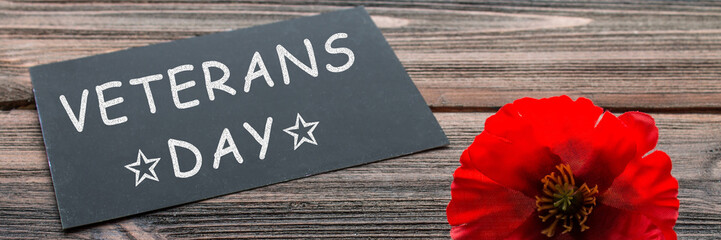 the text thank you veterans written in a chalkboard and red poppy on a rustic wooden background. banner