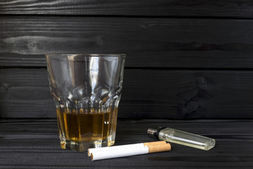  a glass with alcohol, two cigarettes, a lighter, on a table of dark wood
