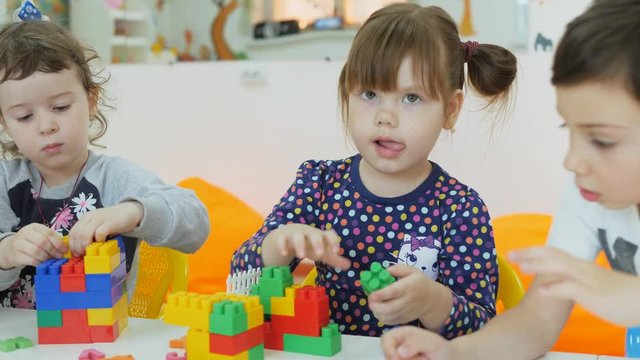 Children's playroom. Emotions of young children during recreational activities. Boys and girls play with multi-colored plastic blocks, sitting at the table.