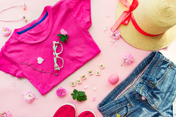 Female planning concept for summer trip clothing and accessories. Fashion style -T-shirt, denim shorts, sneakers, sun glasses, straw hat, lip balm, headphones and flowers on pink background.