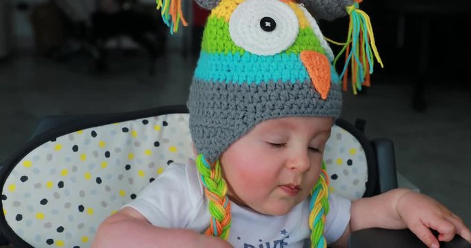 Beautiful Baby With A Funny Colored Wool Hat On The Head, Cute Six Month Old Baby Boy In High Chair. Close Up View - 4K Resolution

