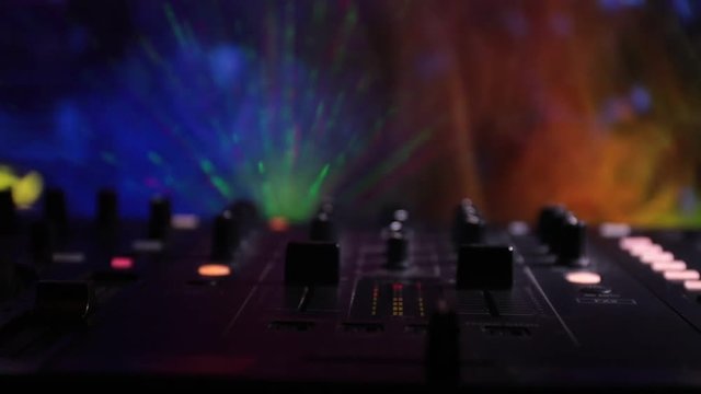 Slider shot. In selective focus of Pro dj controller.The DJ console deejay mixing desk at music party in nightclub with colored disco lights. Close up view