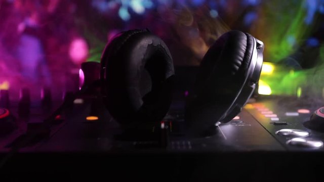 Slider shot. In selective focus of Pro dj controller.The DJ console deejay mixing desk at music party in nightclub with colored disco lights. Close up view