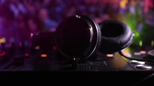 Slider shot. In selective focus of Pro dj controller.The DJ console deejay mixing desk at music party in nightclub with colored disco lights. Close up view