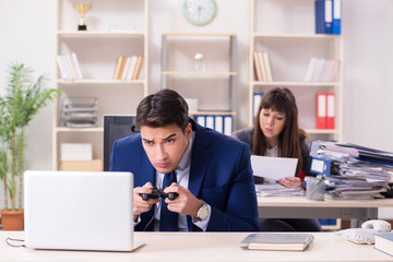 Man playing games in office while colleague is busy