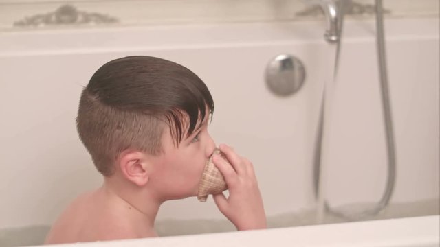 Two little boys having fun with seashell while taking bath in bathtub