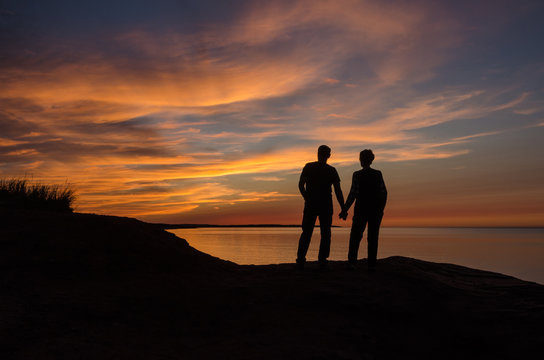 Backlit Couple on large rock overlooking colorful maritime sunset