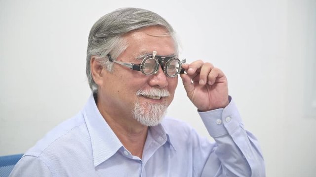 Happy senior man trying out his lens using Phoropter. Chinese man using a Phoropter to be able to see clearly, smile at the end. Medical concept.