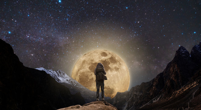 a man standing on mountain peak at night, and full moon on night sky full of stars
