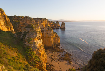 Coastline at sunrise in Algarve Portugal. Secluded empty sandy beach with rocks and nearby cliffs at sunrise.