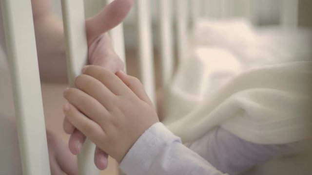 The parent holds the hand of a small child sleeping in a baby crib. Happy family and her newborn baby together. The concept of motherhood.