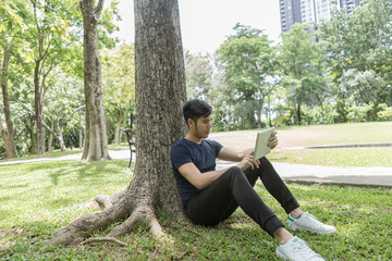 Young man use the tablet and leaning on the tree in the park.