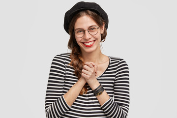 People, positive emotions concept. Attractive French woman being very pleased, keeps hands together, smiles broadly, hears good words about her country, enjoys communication with foreign people