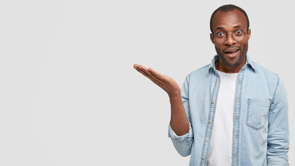 Intelligent dark skinned male with confdent expression, keeps palm raised as demonstrates project...