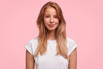 Candid shot of pretty female with long hair, has gentle smile, happy to be praised by boss, stands...