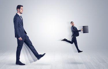 Big man in suit kicking out little himself with simple white wallpaper
