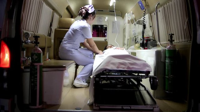 Accident victim inside ambulance at night being treated by nurse. Chinese young female patient laying in bed in ambulance with beautiful female nurse checking her conditions. Sliding dolly shot.
