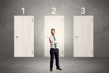 Businessman in grey room with three numbered white  door behind his back
