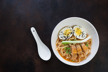 Chicken ramen noodles served in a white bowl, flat-lay over brown metal background with copy space, horizontal shot