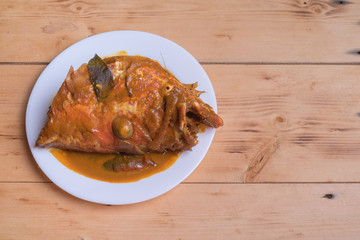 Malaysian red fish head curry in white plate over the pine wood