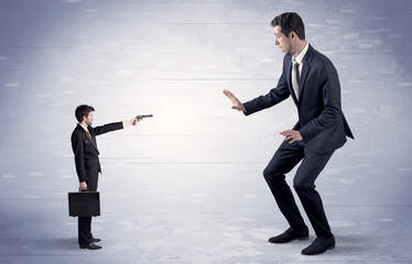 Tiny businessman with gun shooting giant fearful businessman
